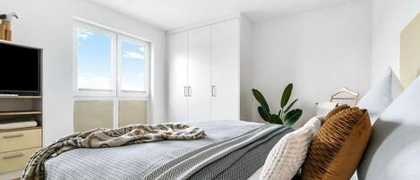 A modern bedroom with a bed, a TV, a window, and a plant.