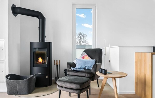 A modern living room with a black wood-burning stove, a comfortable leather armchair, a small round wooden table, and a black storage basket. - Gorgeous apartment in Olpenitz (Olpenitz)