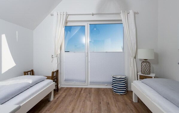 A room with two beds, a window with curtains, a lamp, and a striped bag on the floor. - Beach front apartment in Olpenitz (Olpenitz)