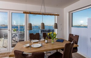 A dining area with a wooden table, brown chairs, and a view of the sea through large windows. - Beach front apartment in Olpenitz (Olpenitz)