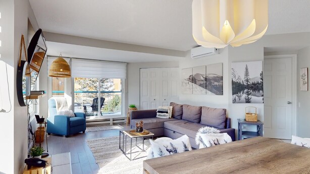 Un salon moderne avec un canapé, une table basse et une table à manger en bois. Une grande fenêtre offre une vue sur l’extérieur.