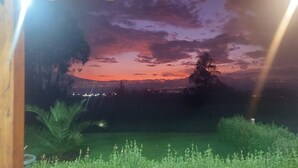 Een kamer met uitzicht op een zonsondergang boven een stadsgezicht, een houten plafond en een groen gazon.