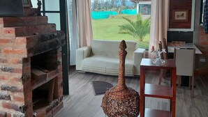 Een woonkamer met een metselwerk open haard, een bank, een eettafel en uitzicht op een groen veld.