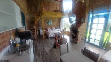 Een rustiek chalet interieur met een slaapkamer op de entresol, een eethoek en een keuken.