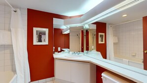 A modern bathroom with red walls, a large mirror, a white sink, and a shower area.