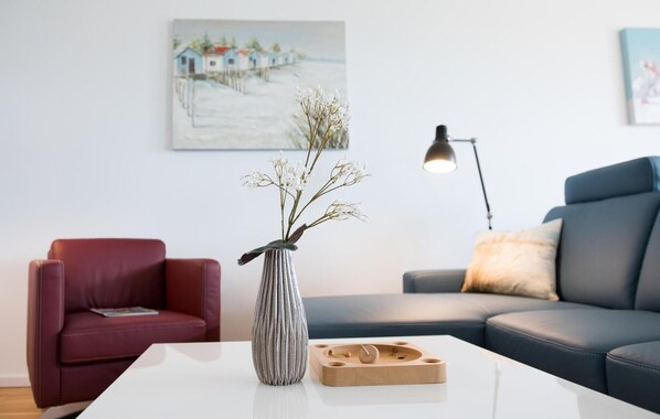 A modern living room with a red chair, a blue sofa, a white coffee table, and a vase with white flowers. - Lovely home in Olpenitz with sauna (Olpenitz)
