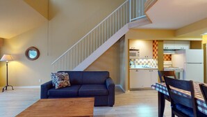 A living room with a dark blue sofa, a wooden coffee table, and a staircase leading to a kitchen with a checkered backsplash. - 1-511 : Condo - 1 bedroom - sleeps 4 (Beaupré)