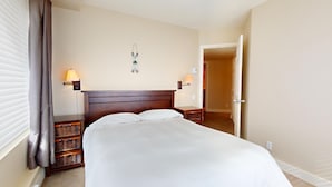 A hotel room with a large bed, two bedside tables, a wall-mounted lamp, and a door leading to another room.