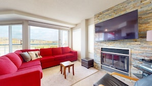 A modern living room with a red sofa, a fireplace, and a large TV mounted on a stone wall.