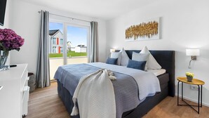 Et moderne soveværelse med en stor seng, et natbord med lampe, og udsigt ud.