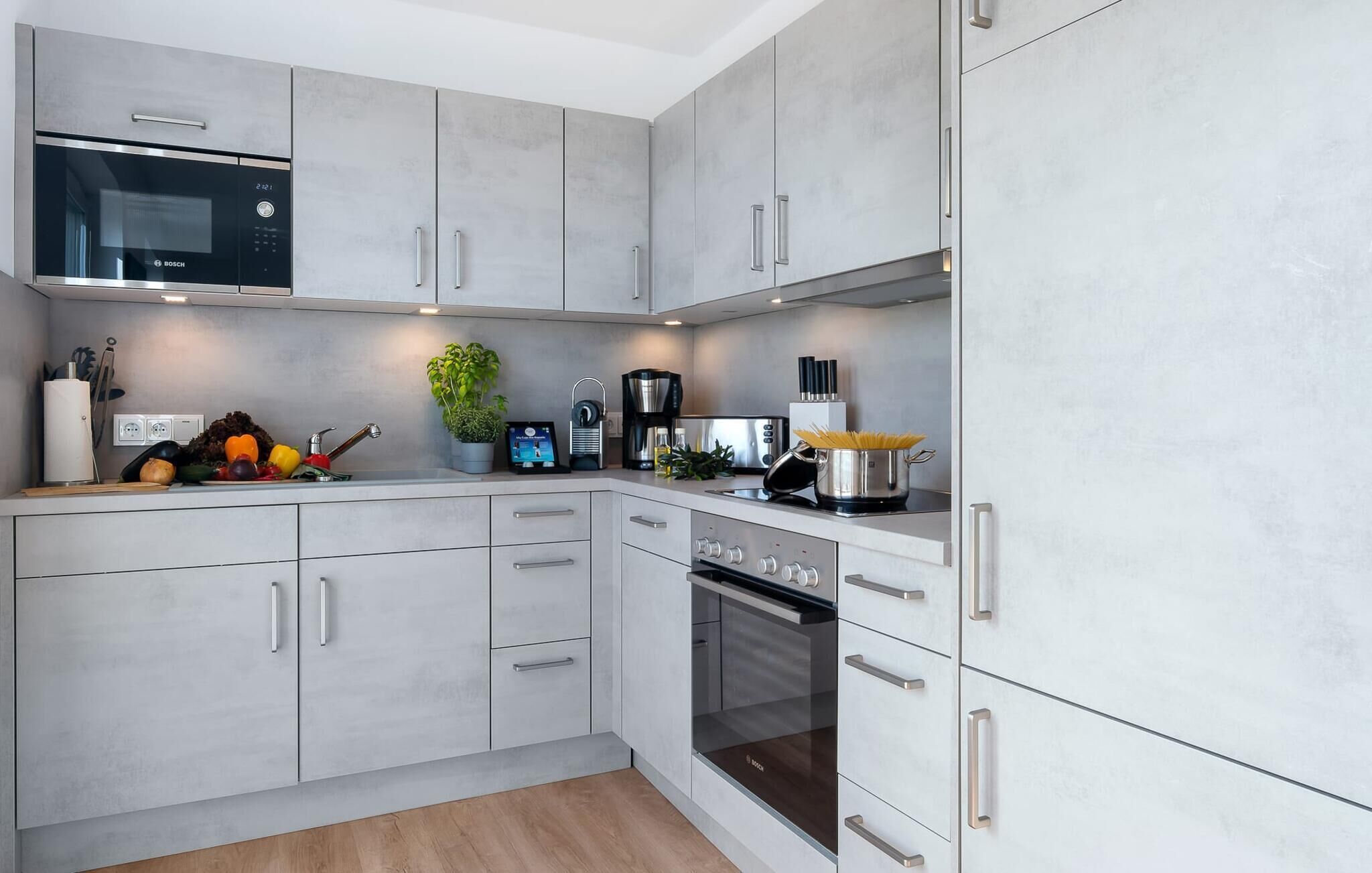 A modern kitchen with grey cabinets, a Bosch microwave, a coffee machine, and a stove.