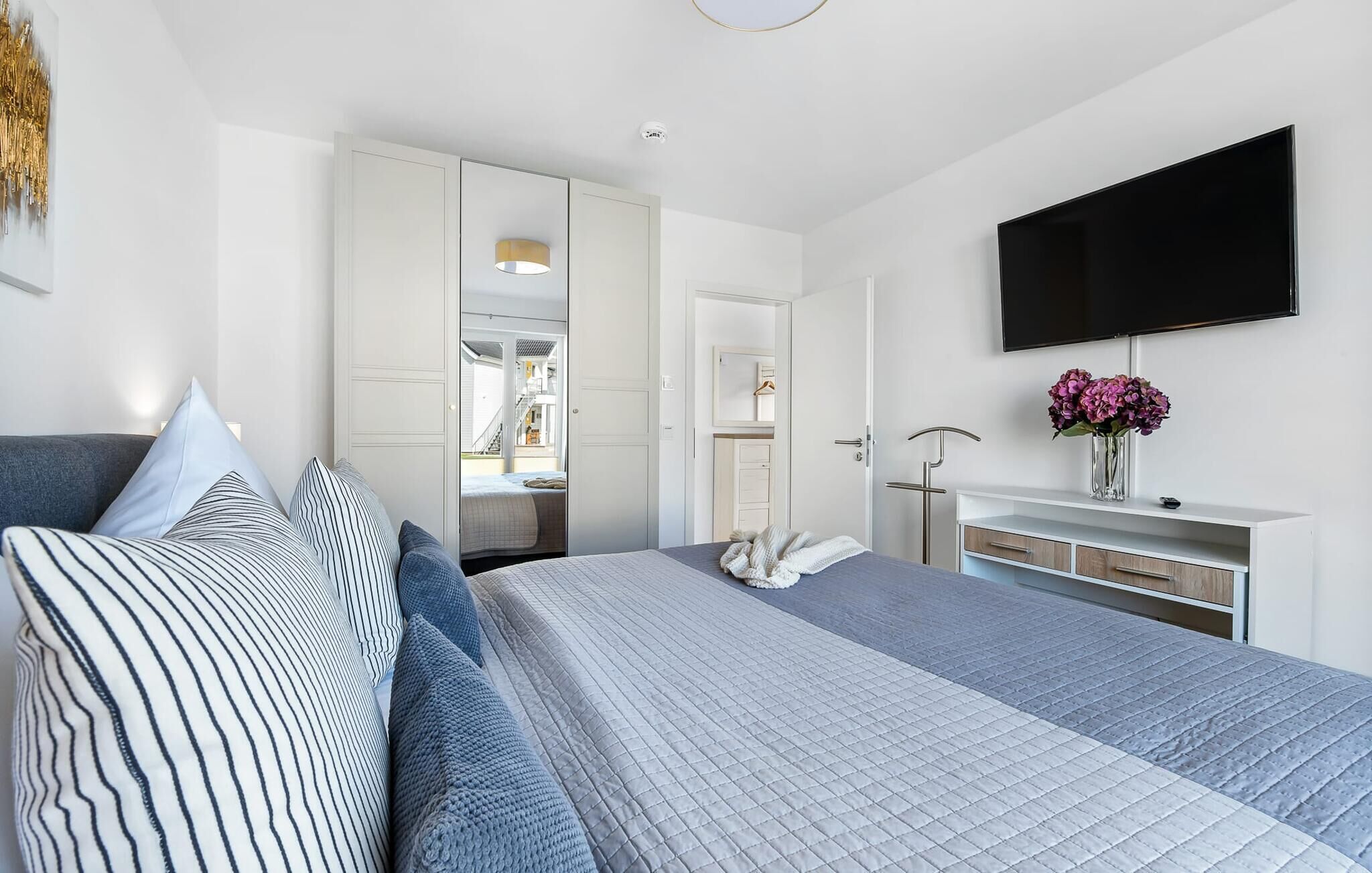 A modern bedroom with a bed, bedside table, TV, and a view into the bathroom.