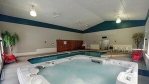 A large indoor swimming pool with a hot tub, surrounded by red chairs, and a wooden cabinet in the background.