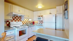 Une cuisine de taille réduite, avec des meubles blancs, une cuisinière, un four à micro-ondes et un réfrigérateur.