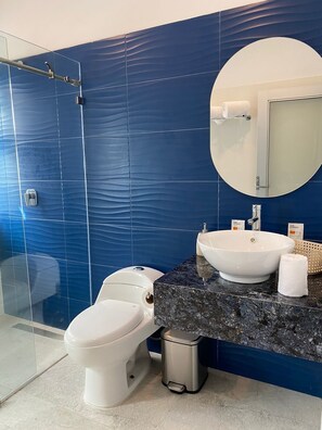A modern bathroom with a blue tiled wall, a round mirror, a white sink, and a toilet. - Hotel BG Wellness & Spa Boca del Rio Veracruz (Boca del Río)