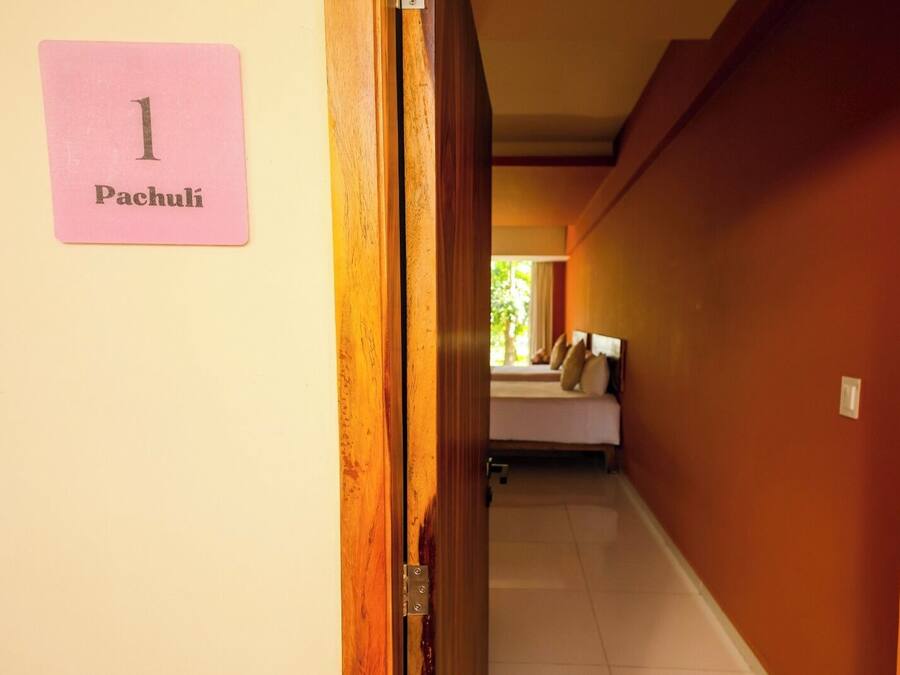 A hallway with a sign reading "1 Pachuli" on the left, leading to a room with a bed and a window.