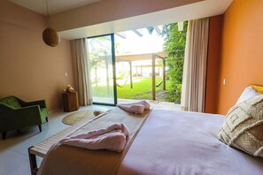 A bedroom with a large bed, a green chair, and a view of a garden through a sliding glass door.