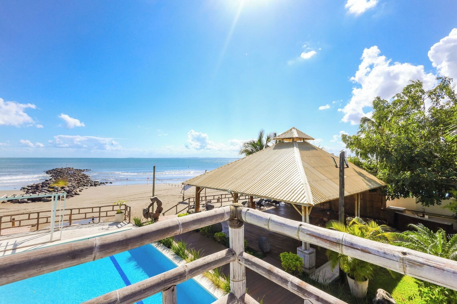 A beachside resort with a pool, a beach area, and a thatched-roof structure.