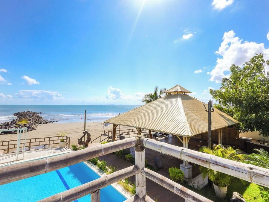 A beachside resort with a pool, a beach area, and a thatched-roof structure.