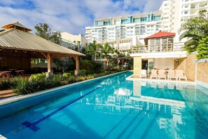 A swimming pool with lounge chairs and a covered area, surrounded by greenery and a multi-story building with balconies. - Hotel BG Wellness & Spa Boca del Rio Veracruz (Boca del Río)