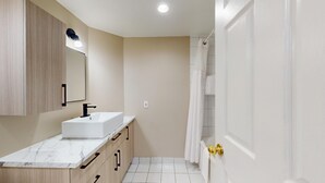Un baño con lavamanos blanco, armarios de madera, un espejo y cortina de ducha.