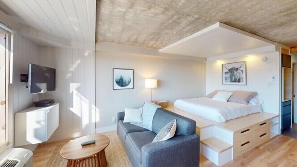 Una habitación de hotel moderna con cama, sofá, televisor y obras de arte.