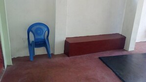 Una habitación con una silla de plástico azul, un banco rojo y un tapete negro en el suelo.