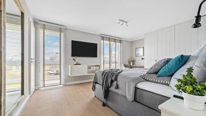 Une chambre à coucher moderne avec un grand lit, un téléviseur fixé au mur et une porte-fenêtre coulissante donnant sur un balcon.