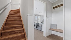 Un escalier en bois mène à une chambre qui contient un lit, un banc et un porte-manteau.