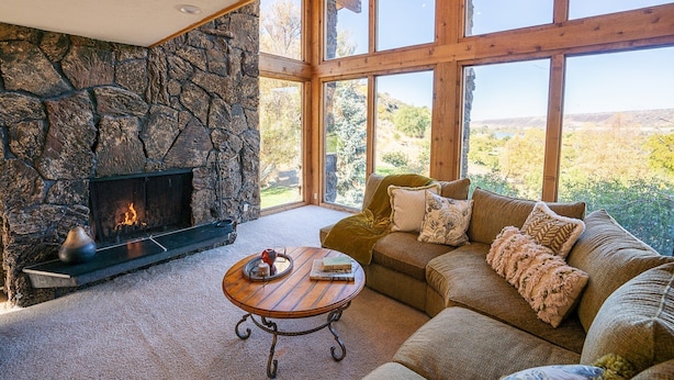 Una sala de estar acogedora con chimenea de piedra, un sofá cómodo y ventanas amplias que ofrecen vistas al exterior.