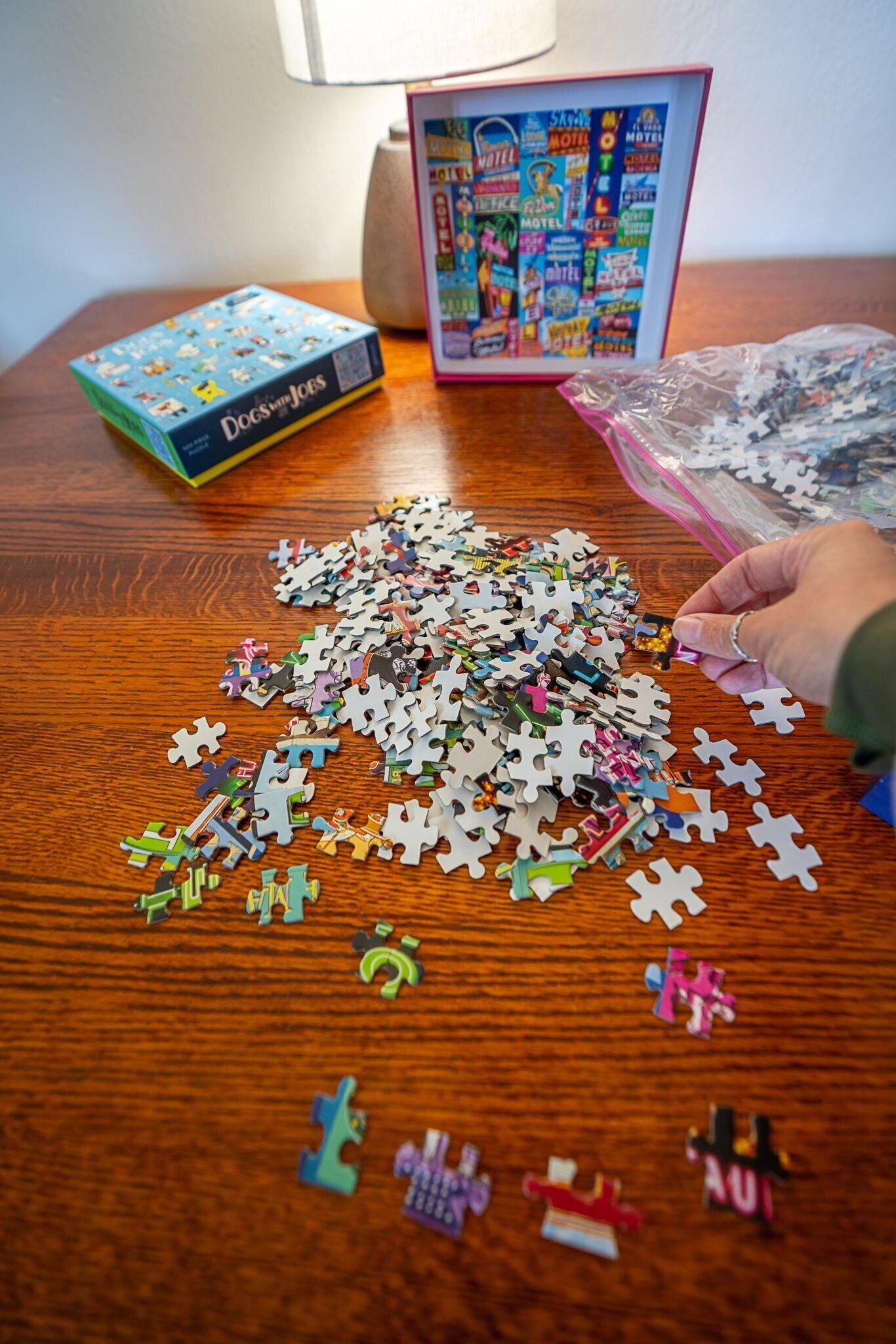 A wooden table with a puzzle in progress, a puzzle box, and a partially used puzzle bag.