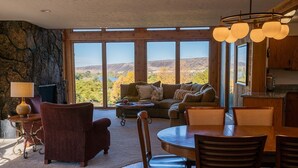 Amplia sala de estar con un ventanal que ofrece vistas a las montañas, una zona de estar acogedora con chimenea y una mesa de comedor de madera.