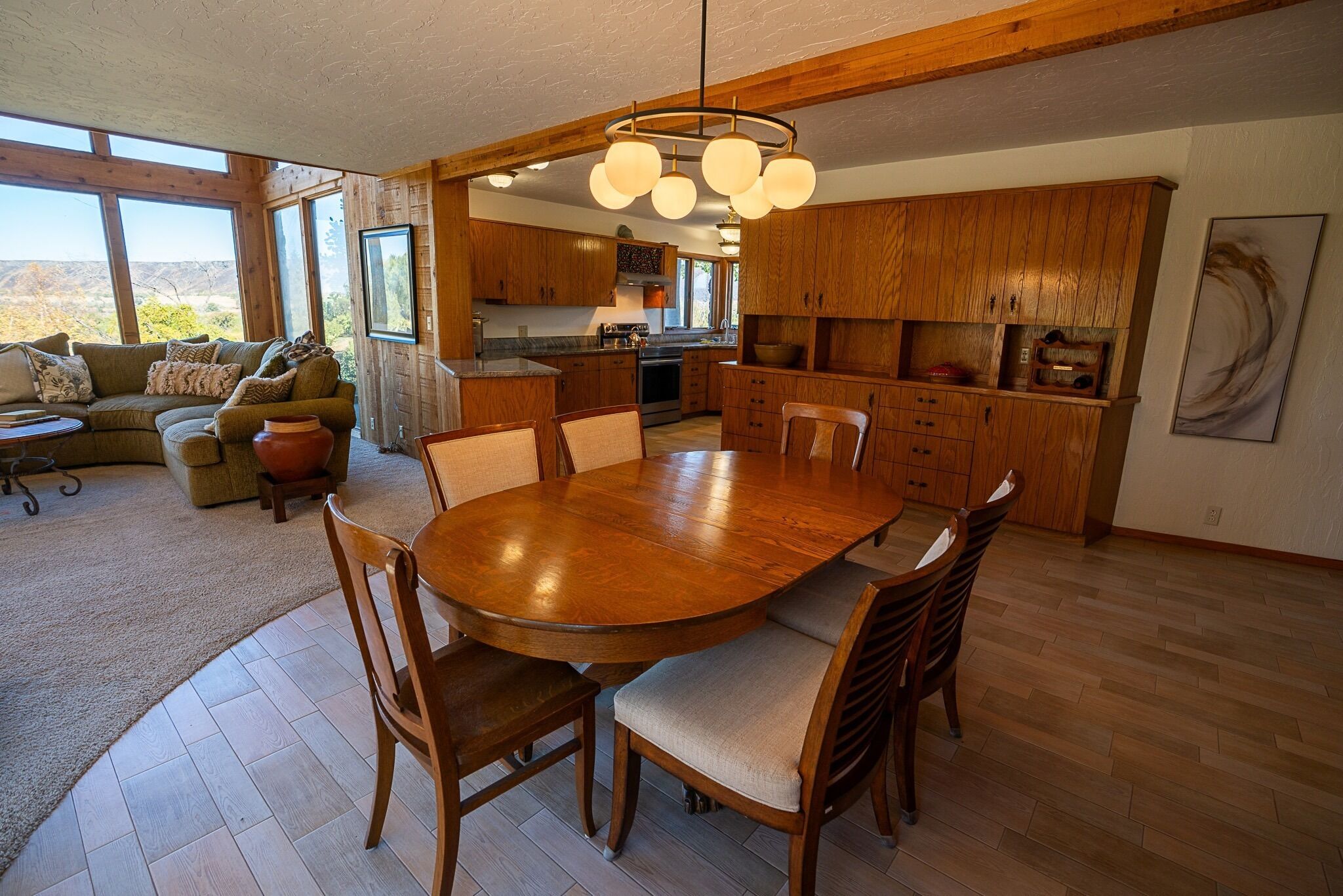 A spacious living area with a wooden dining table and chairs, a sofa, and a view of the mountains through large windows.