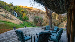 Una terraza de madera con muebles de exterior, una cascada al fondo y una ladera.