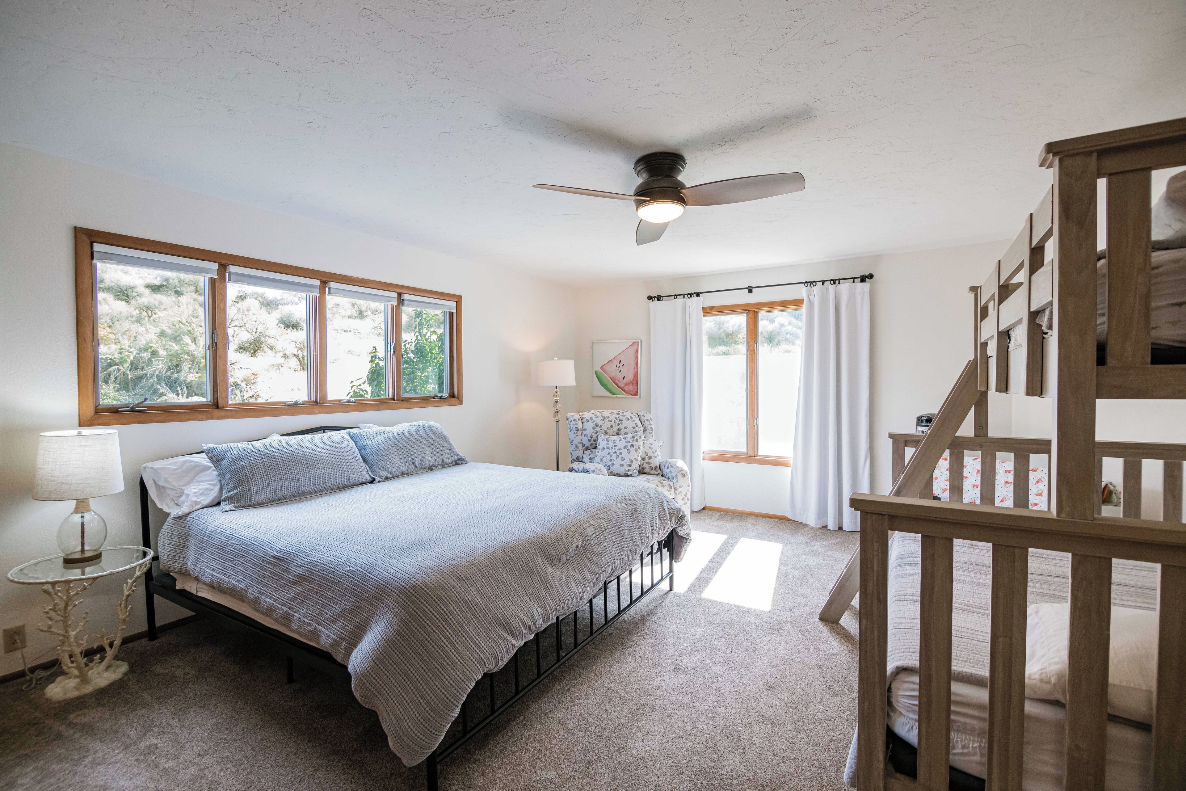 Un dormitorio con cama, ventilador de techo, ventana y escalera.