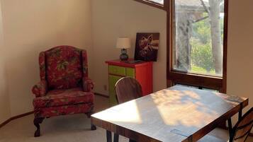 A dining area with a wooden table and chairs, a floral armchair, a small red cabinet with a lamp, and a painting of a dog.