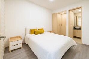 Ein Schlafzimmer mit Bett, Nachttischen, einem Kleiderschrank und einem durchgehenden Türbogen erreichbaren Badezimmer.