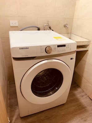 Eine Samsung Digital Inverter Waschmaschine in einem Badezimmer mit gefliesten Wänden, einem Waschbecken und einem Holzboden.
