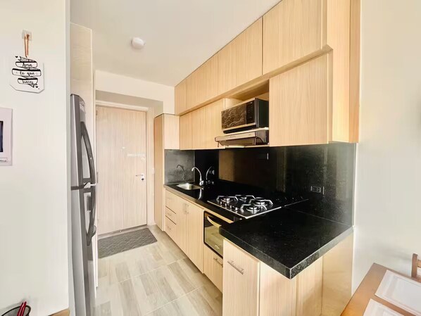 A modern kitchen with wooden cabinets, a black countertop, a stainless steel refrigerator, and a microwave. - Close to the airport and terminal; modern and quiet. (Bogotá)