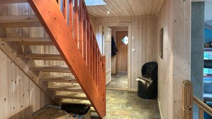 Interior de madera con una escalera, una silla y una puerta que da a otra habitación.
