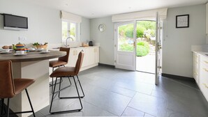 Eine moderne Küche mit Kochinsel, weißen Schränken und einem großen Schiebeglastür zum Garten.