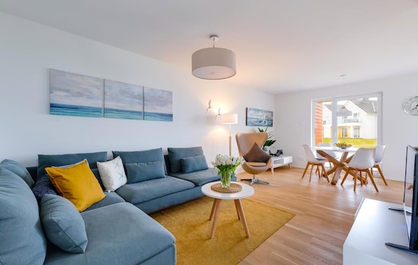 Un salon moderne avec un canapé bleu, une petite table ronde et un coin repas comprenant une table et des chaises blanches.