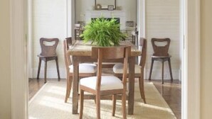 Een eethoek met een houten tafel en stoelen, een potplant en een witte open haard.