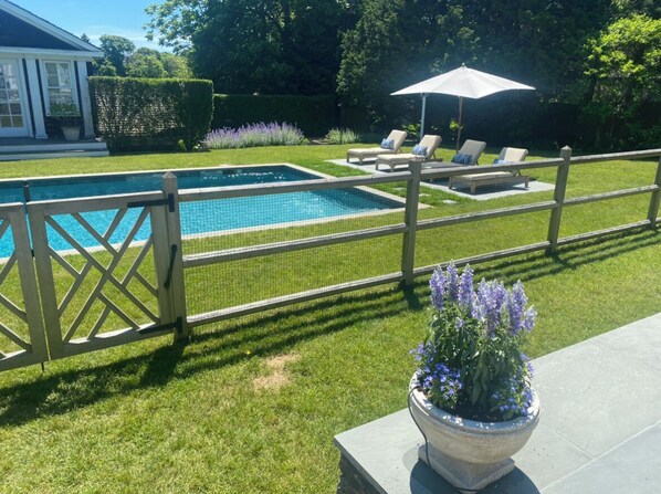 Une piscine entourée d’une clôture en bois, avec des chaises longues et un pot de fleurs.