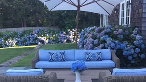 Een rieten bank met blauwe kussens en een bijpassende tafel, geplaatst op een terras met een grote parasol.