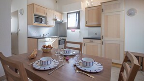 Une cuisine compacte dotée de meubles en bois, d’un four à micro-ondes et d’un coin repas aménagé pour quatre personnes, avec assiettes, couverts et verres.