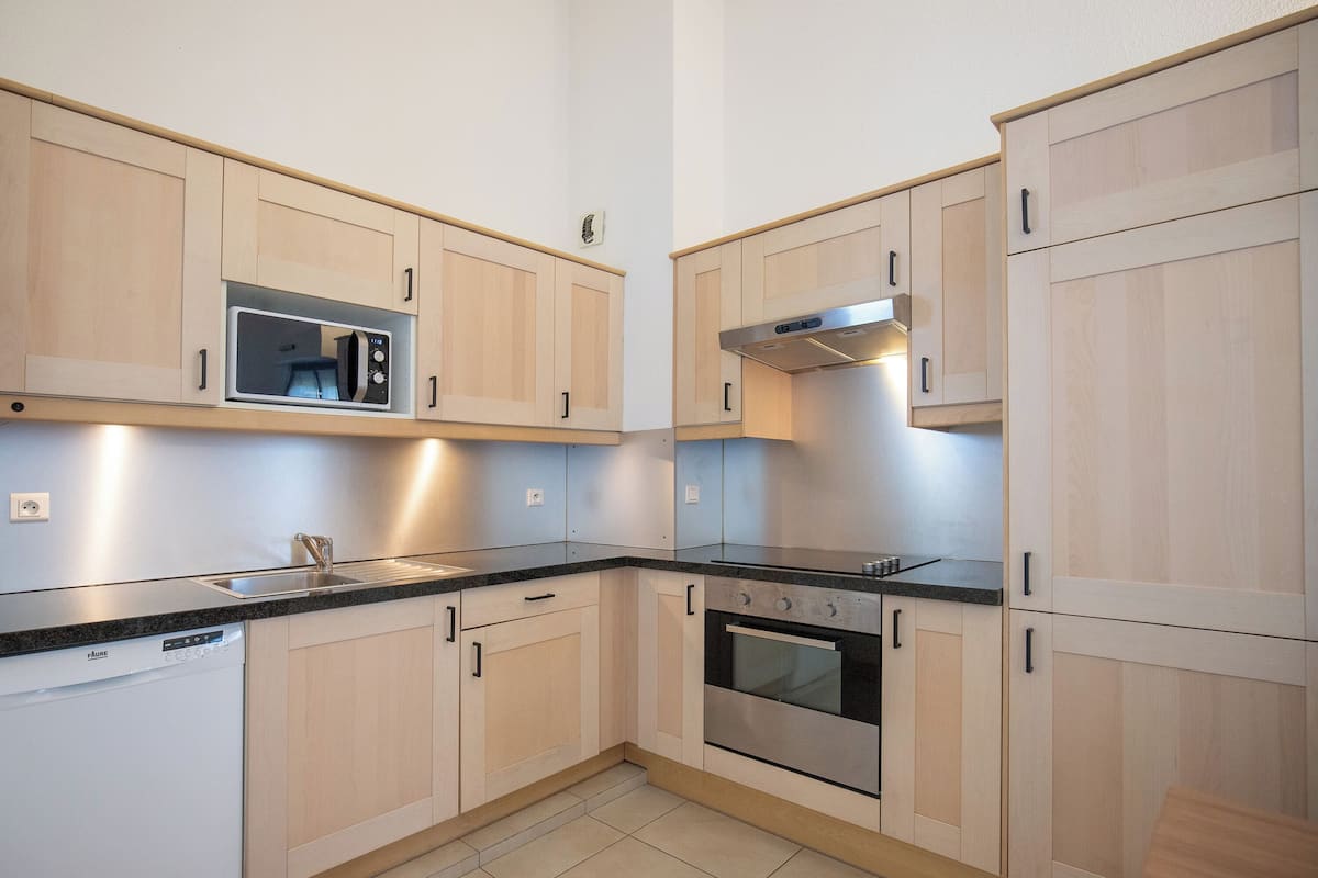 A kitchen with light wood cabinets, a stainless steel microwave, a built-in oven, and a dishwasher.
