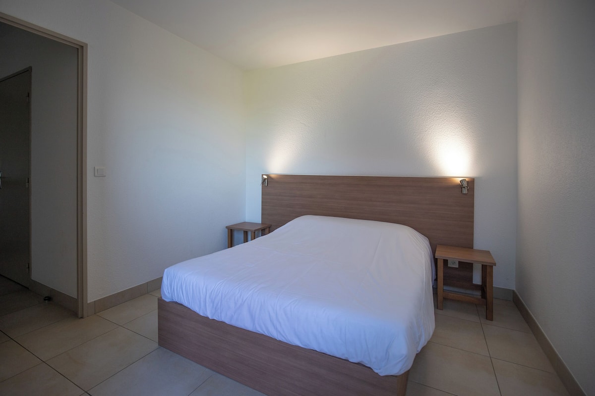 A bedroom with a wooden headboard, a single bed, two bedside tables, and a nightstand.