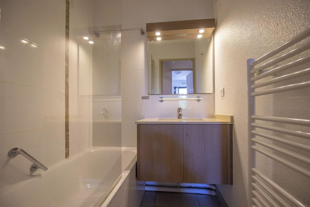 A modern bathroom with a bathtub, a wooden vanity, and a mirror above the sink.