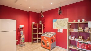 Une pièce aux murs rouges, avec un réfrigérateur Bosch, un présentoir à cartes postales, un petit réfrigérateur pour les glaces et des étagères remplies de bocaux et de tasses.